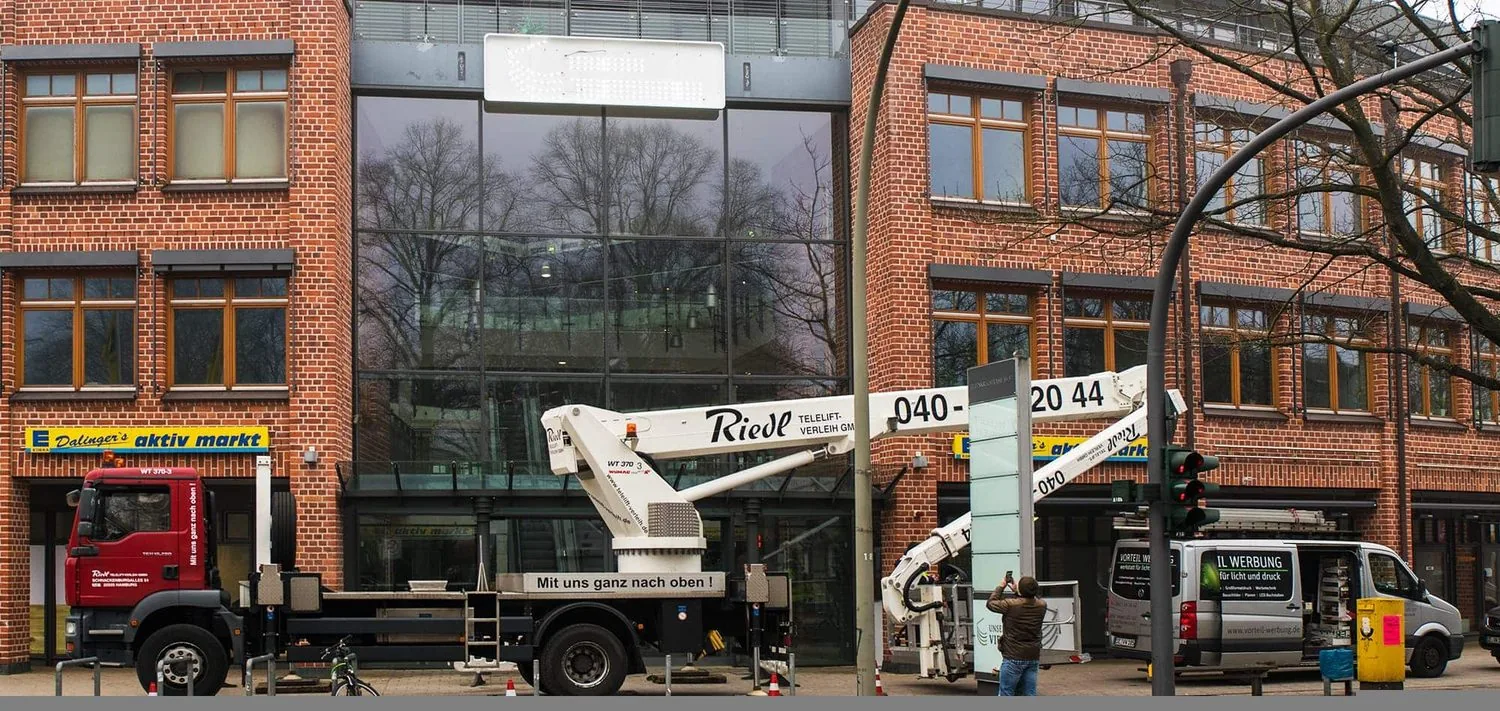 Das Foto zeigt die Montage mit einer Arbeitsbühne von einer Lichtwerbung als Leuchttransparent in Hamburg