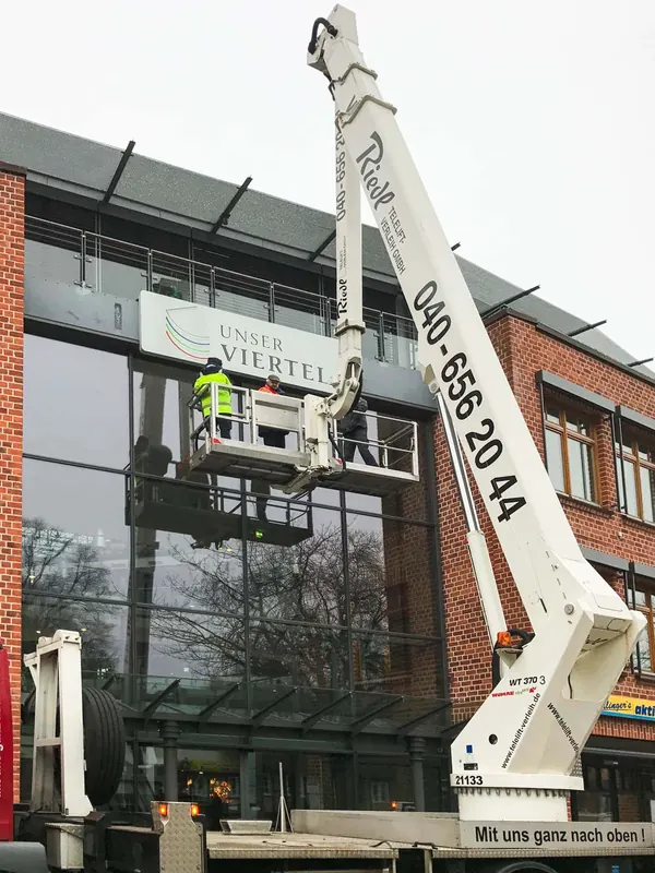 Das Foto zeigt die Montage eines Leuchttransparentes an einer Hausfassade. Buchstaben mit durchgesteckten Plexiglas