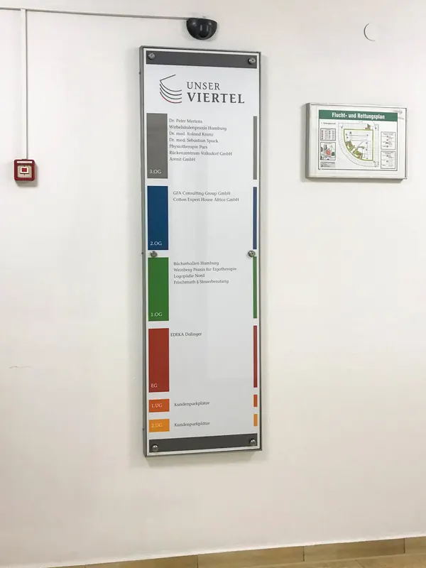 Schilder in Gewebeobjekten als Wegweiser für die Besucher. Glasscheiben mit umlaufender Einfassung aus lackiertem Stahl