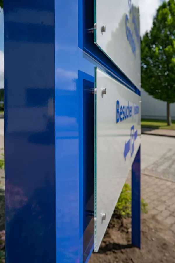 Das Foto zeigt ein Standschild gefertigt aus Aluminium und ESG-Glasscheiben. Das Firmenschild zeigt den Namen und einen Hinweis für die Kundenparkplätze.