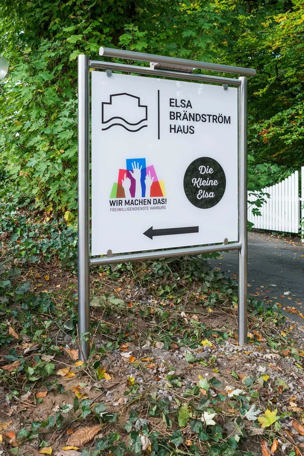 Das Foto zeigt ein Standschild gefertigt aus Edelstahlrohren und einem Werbeschild aus ESG-Glas. Beleuchtet durch eine LED Lichteinheit.