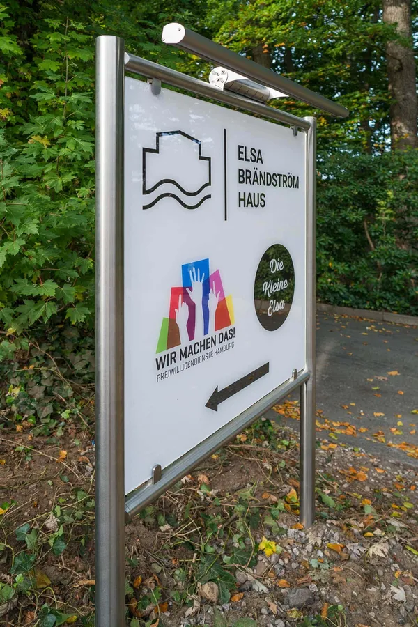 Das Foto zeigt ein Standschild gefertigt aus Edelstahlrohren und einem Werbeschild aus ESG-Glas. Beleuchtet durch eine LED Lichteinheit.