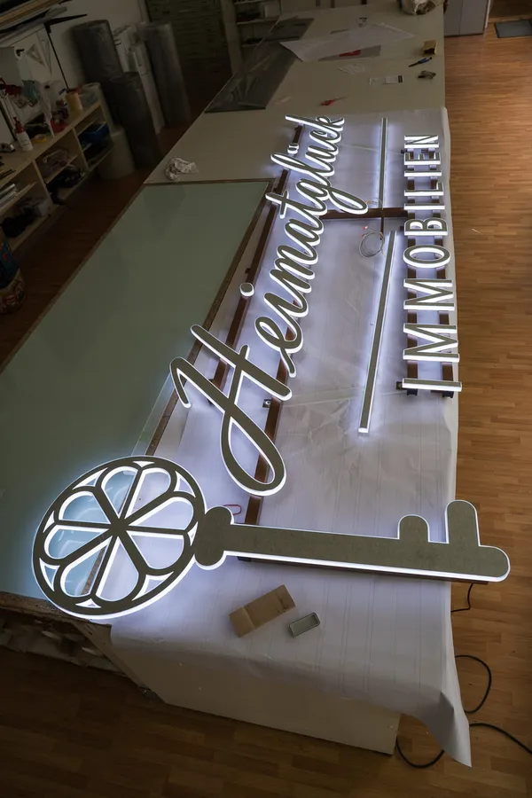 3D Buchstaben aus LED Vollplexi Buchstaben mit gold gebürstetem V2A belegt. Eine Aussenwerbung für Heimatglück Immobilien in Lübeck.
