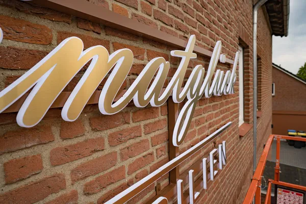 3D Buchstaben aus LED Vollplexi Buchstaben mit gold gebürstetem V2A belegt. Eine Aussenwerbung für Heimatglück Immobilien in Lübeck.